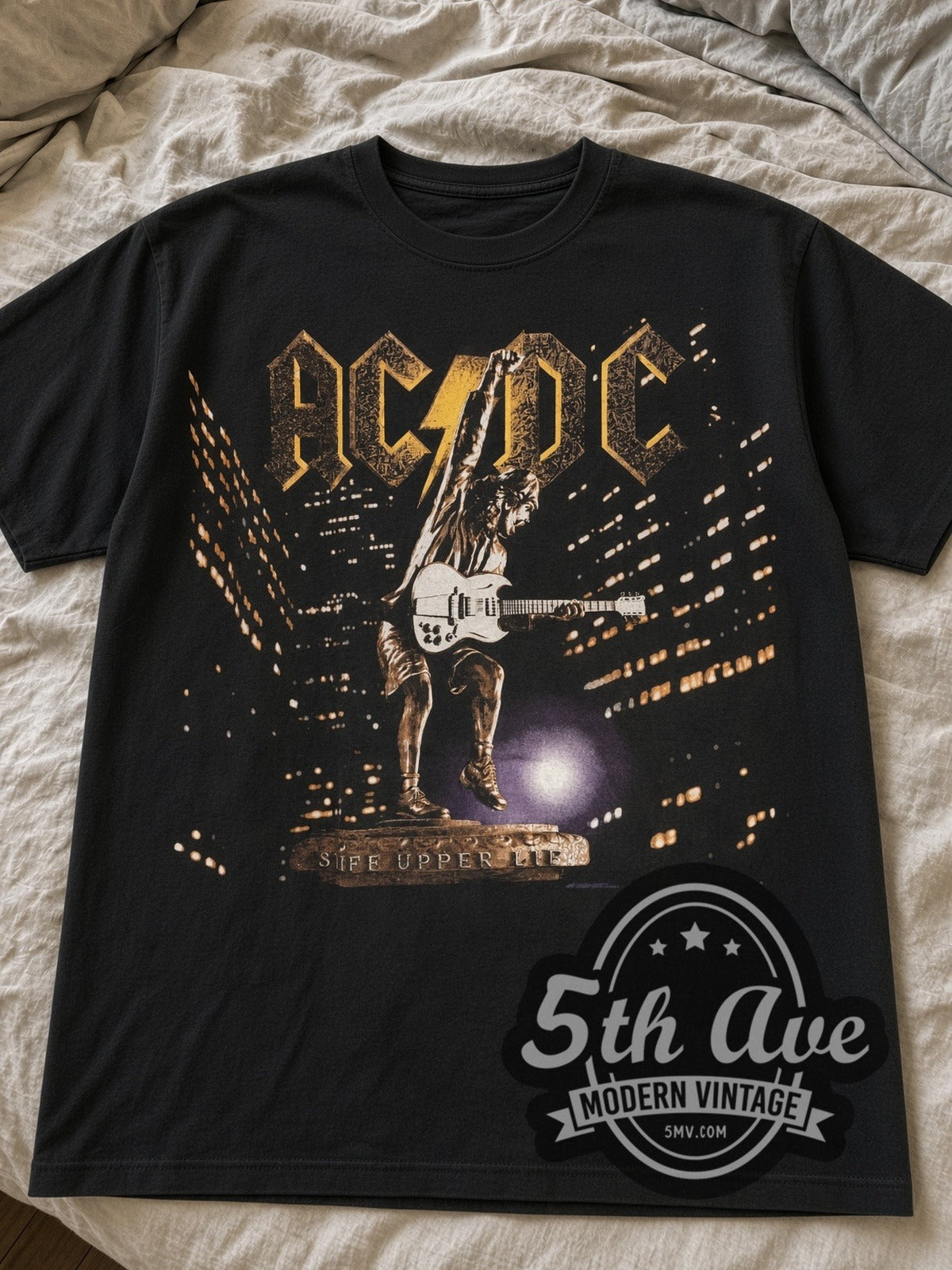Black AC/DC Stiff Upper Lip Angus Statue Tour tee laid flat on linen bed