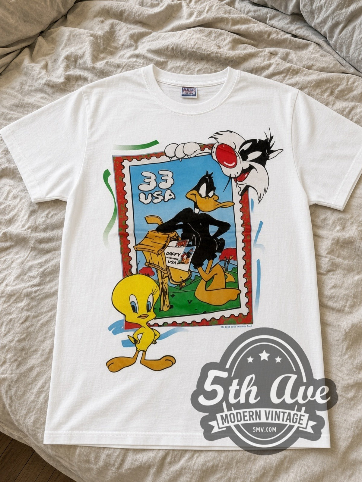 Looney Tunes 33 USA Stamp Tweety Sylvester cartoon tee in white laid flat on a bed, front artwork