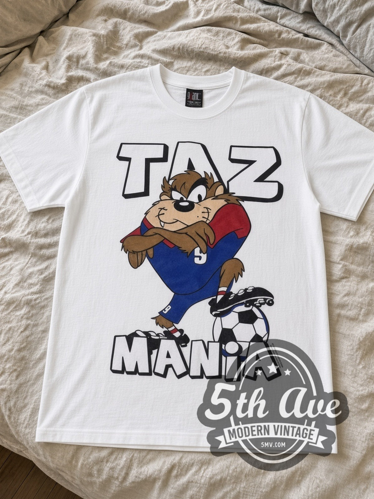 Looney Tunes Taz Soccer Champions cartoon tee in white laid flat on a bed, front artwork