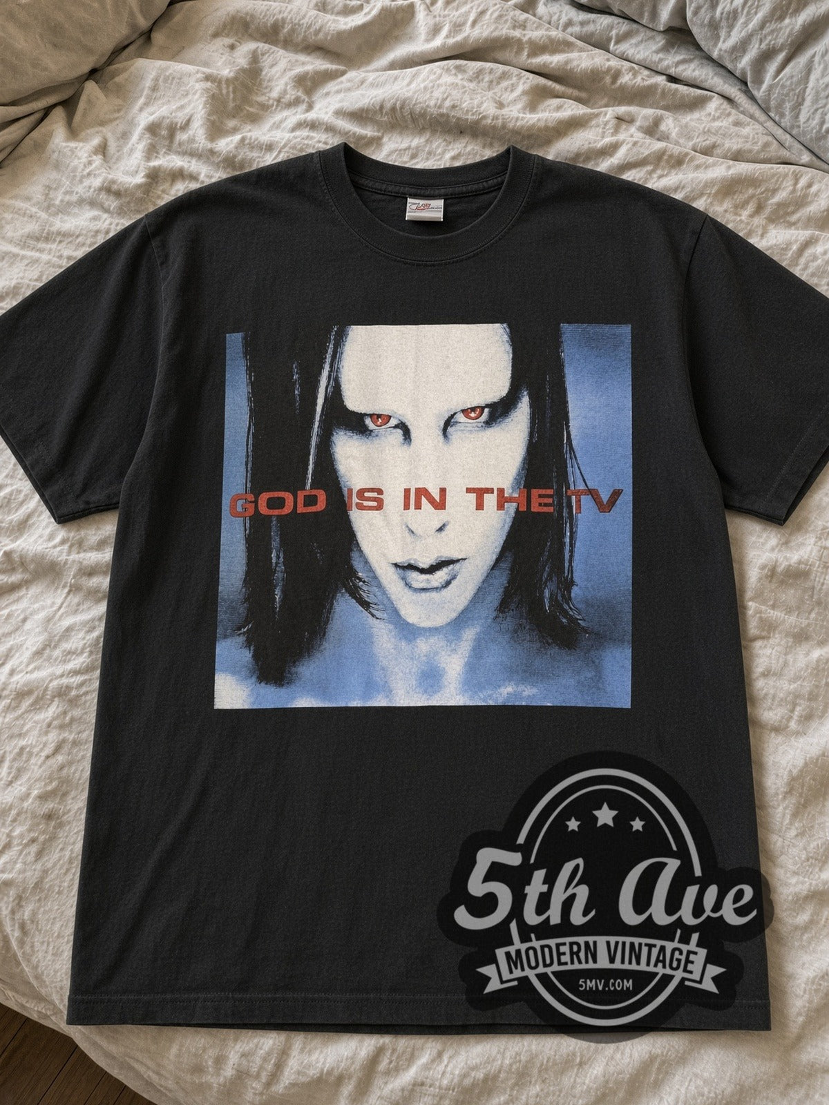 Black Marilyn Manson God Is in the TV Blue Face tee laid flat on linen bed