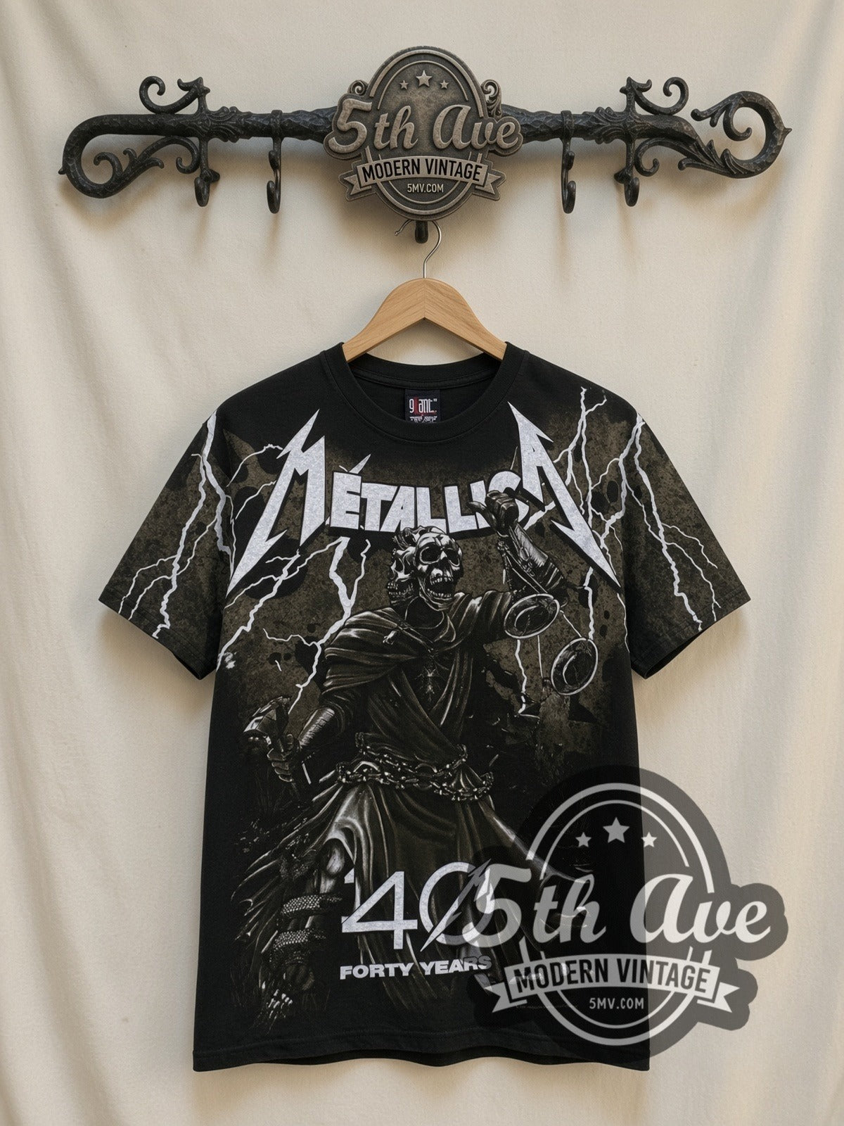Metallica 40 Years Lady Justice all-over-print vintage band t-shirt in black, front view on a display rack