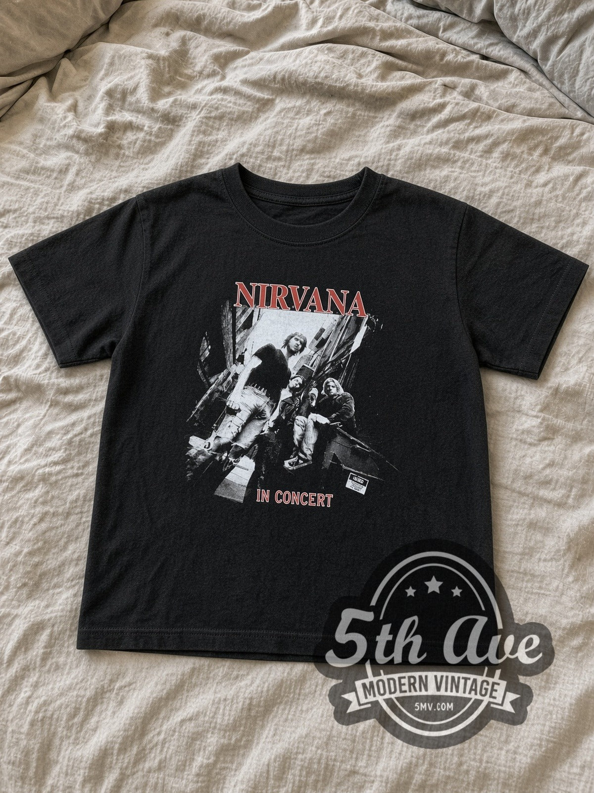 Nirvana In Concert Band Photo kids band tee in black laid flat on a bed, front artwork