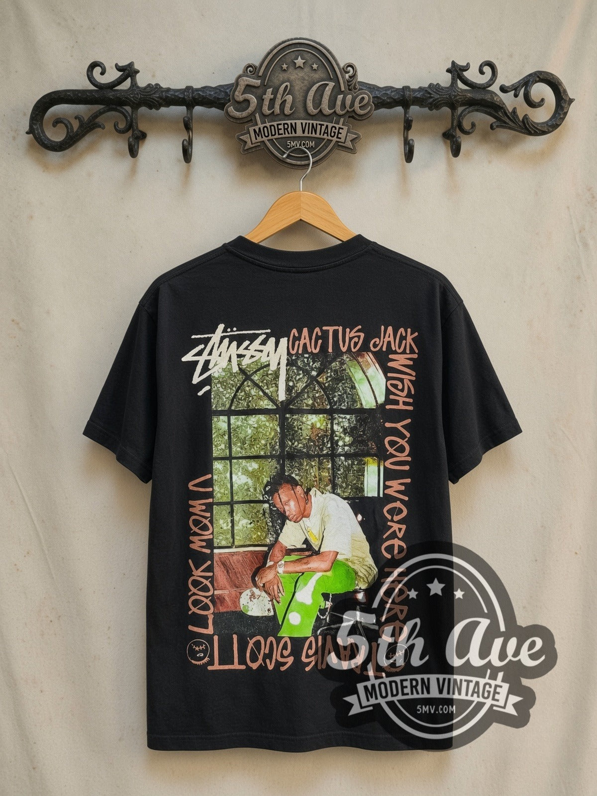 Travis Scott x Stüssy Astroworld graphic tee in black, back view on a display rack