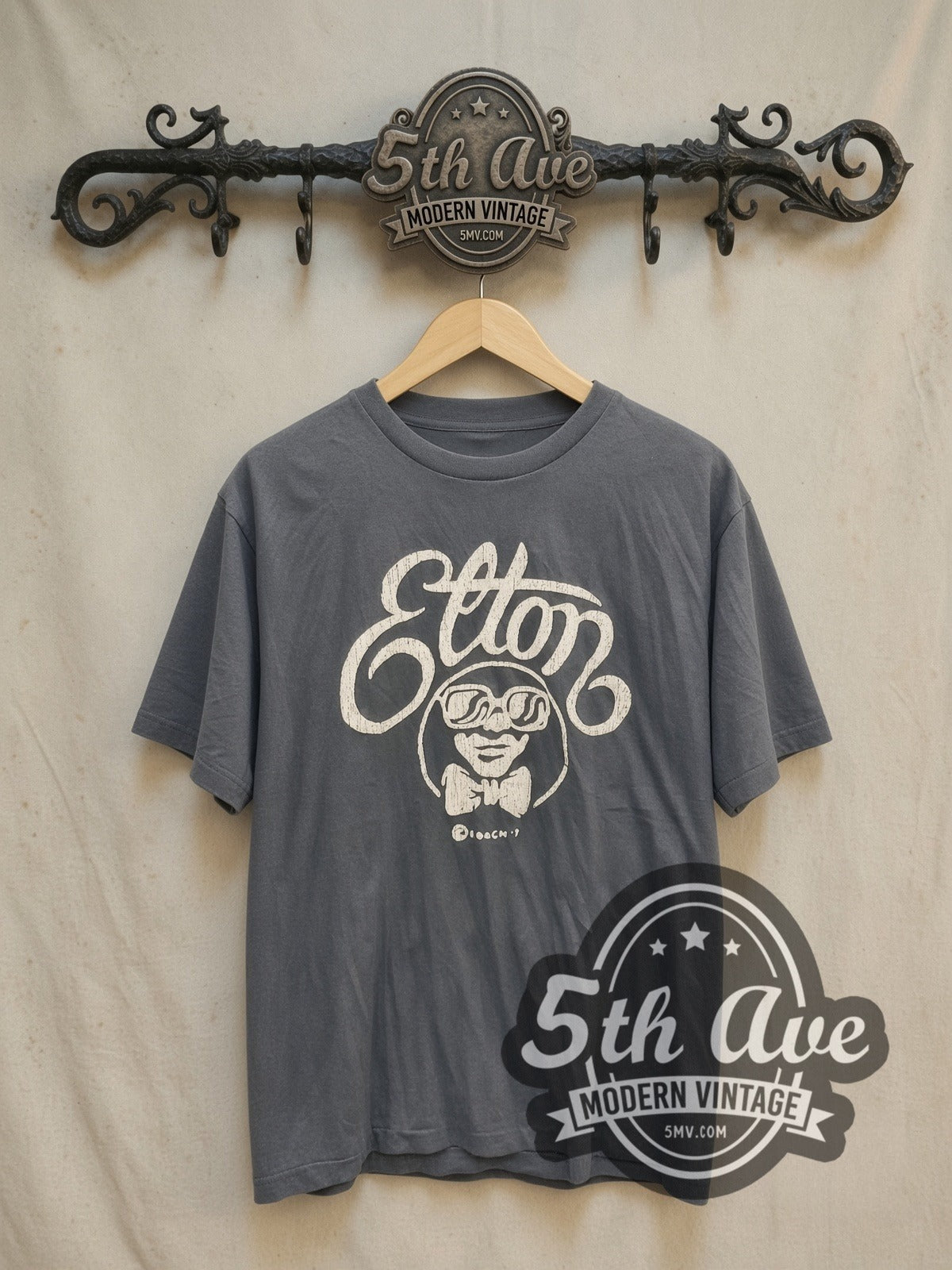 Elton John Elton Script Cartoon vintage band t-shirt, front view on a display rack