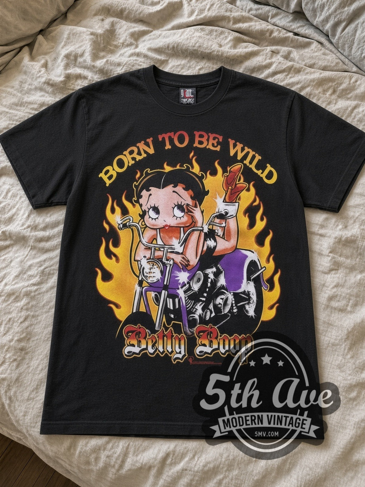 Betty Boop Born to Be Wild Biker cartoon tee in black laid flat on a bed, front artwork