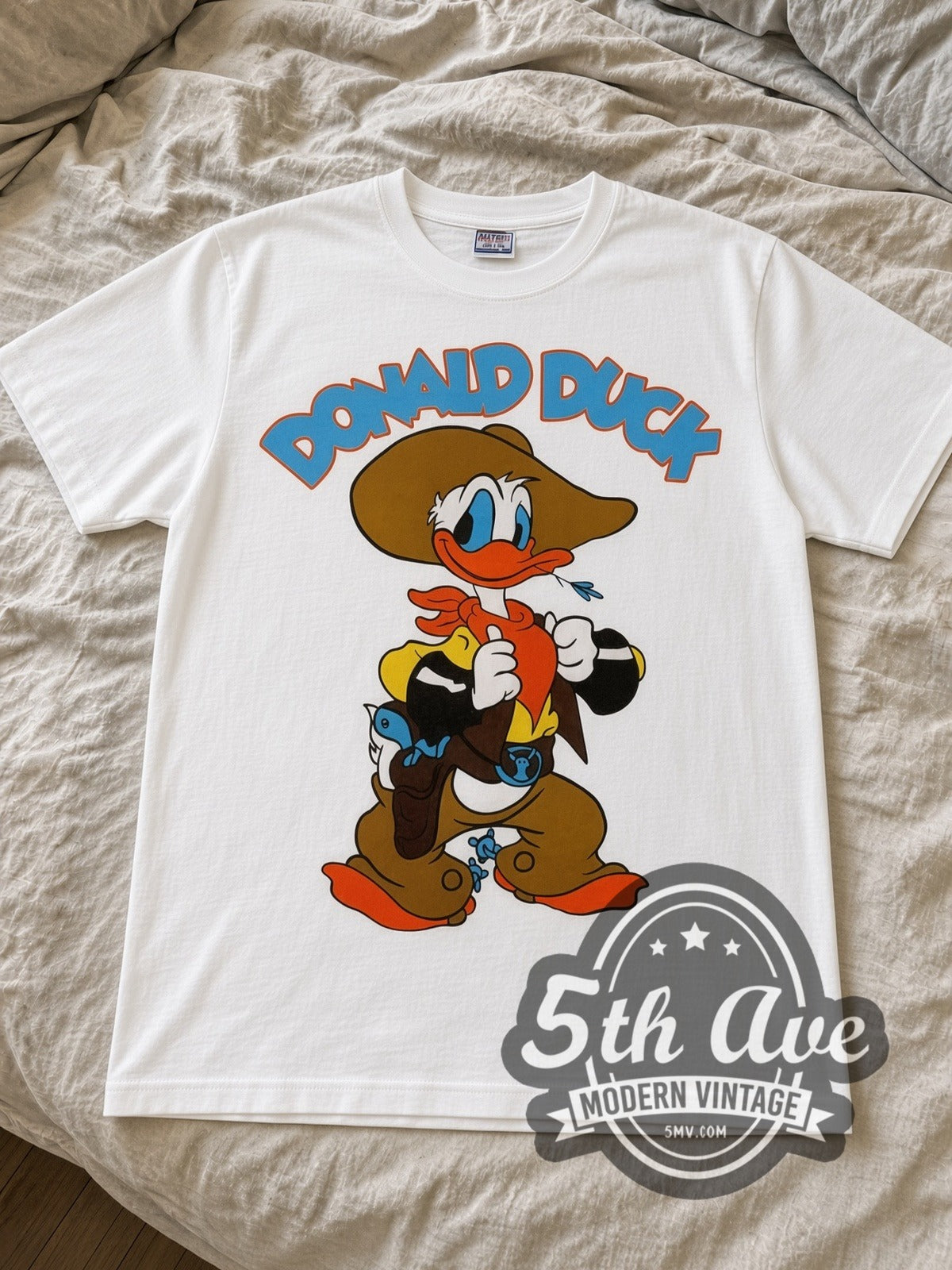 Disney Donald Duck Cowboy and DuckTales Scrooge cartoon tee in white laid flat on a bed, front artwork