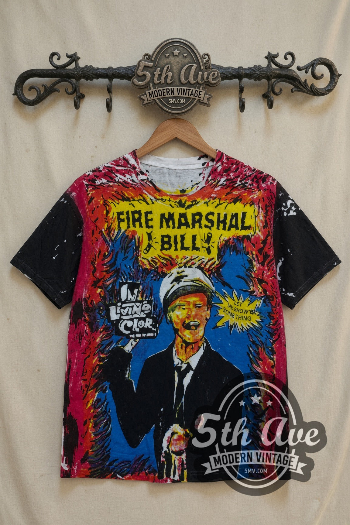 Fire Marshal Bill In Living Color all-over-print t-shirt, front view on a display rack: yellow FIRE MARSHAL BILL banner, flame print, black sleeves