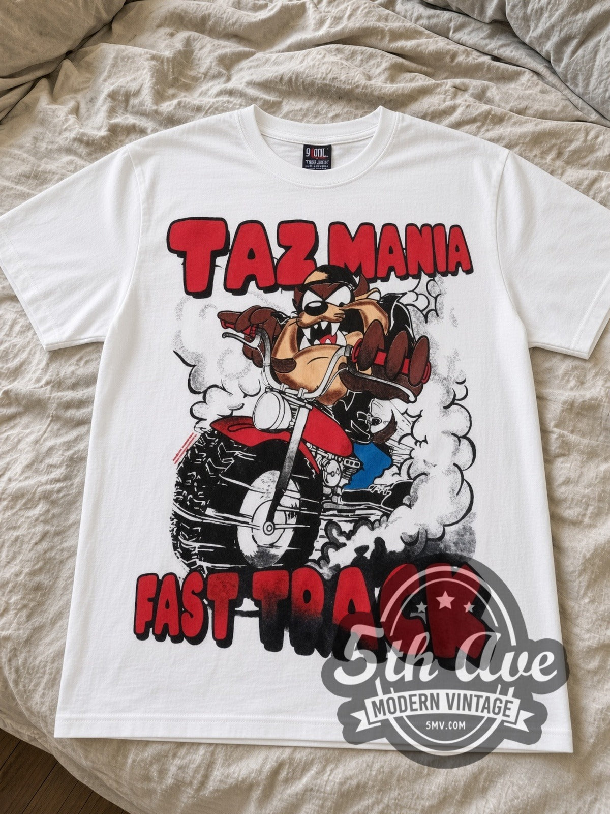 Looney Tunes Taz Fast Track cartoon tee in white laid flat on a bed, front artwork