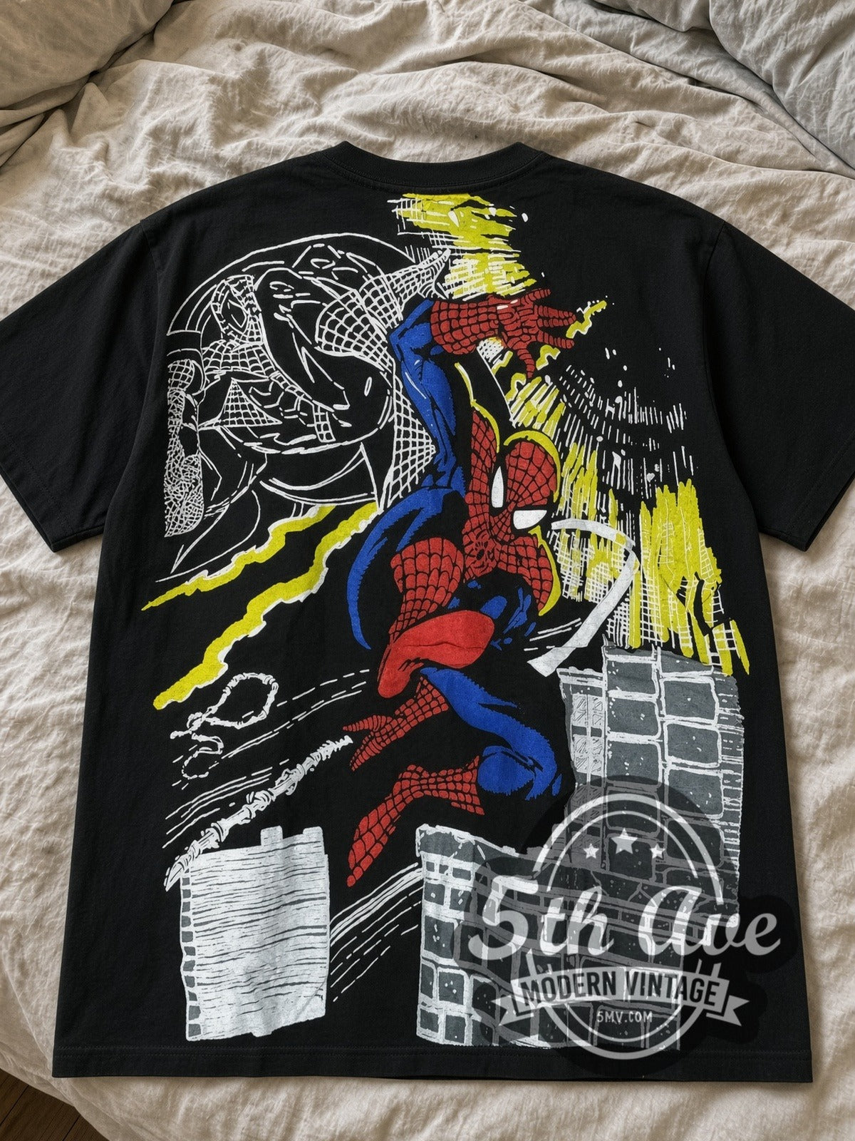 Marvel Spider-Man all-over-print black vintage comic tee laid flat on a bed – full front print with yellow burst and city skyline