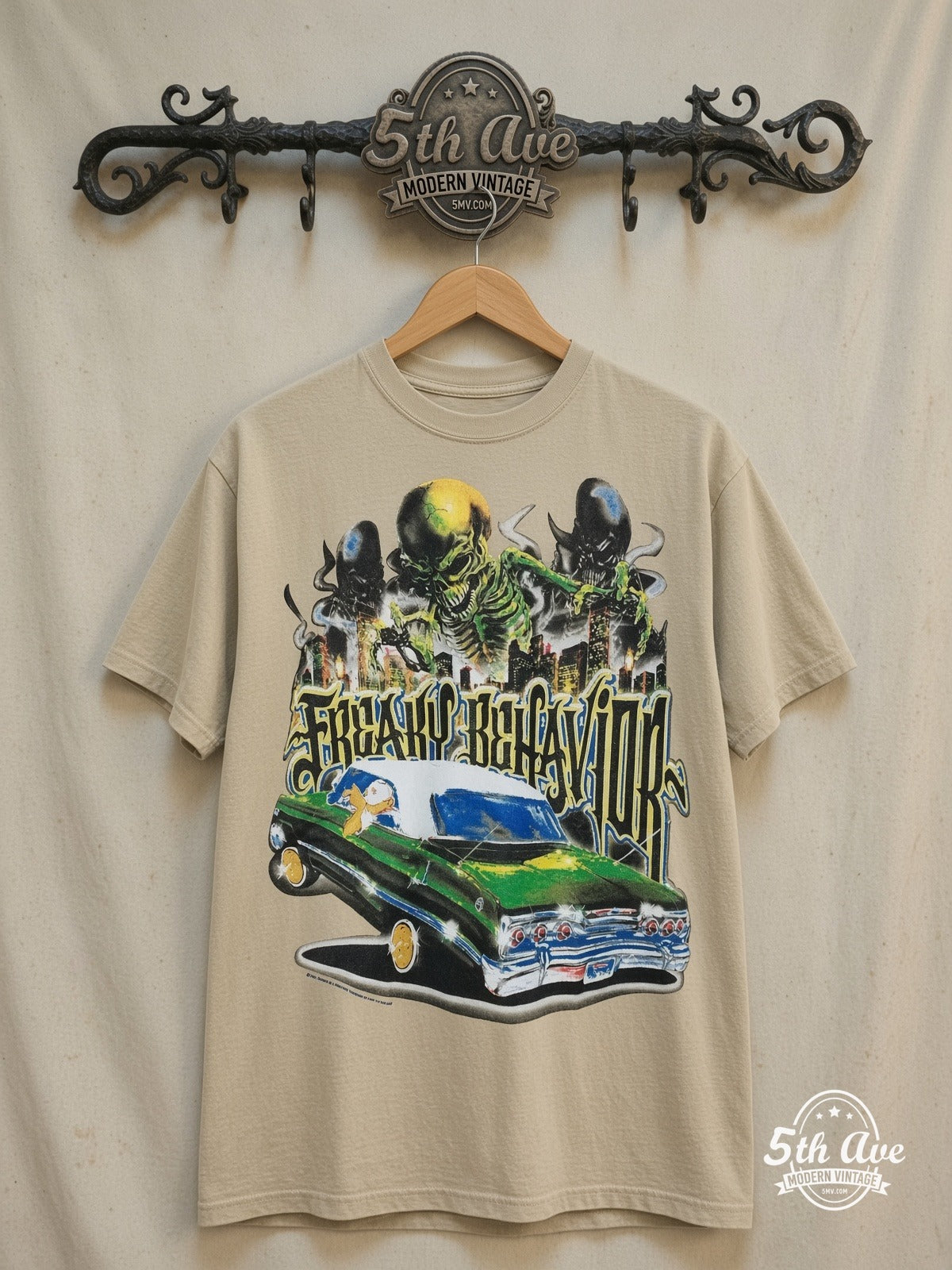 Rollin Hard Freaky Behavior Lowrider graphic tee in sand, front view on a display rack