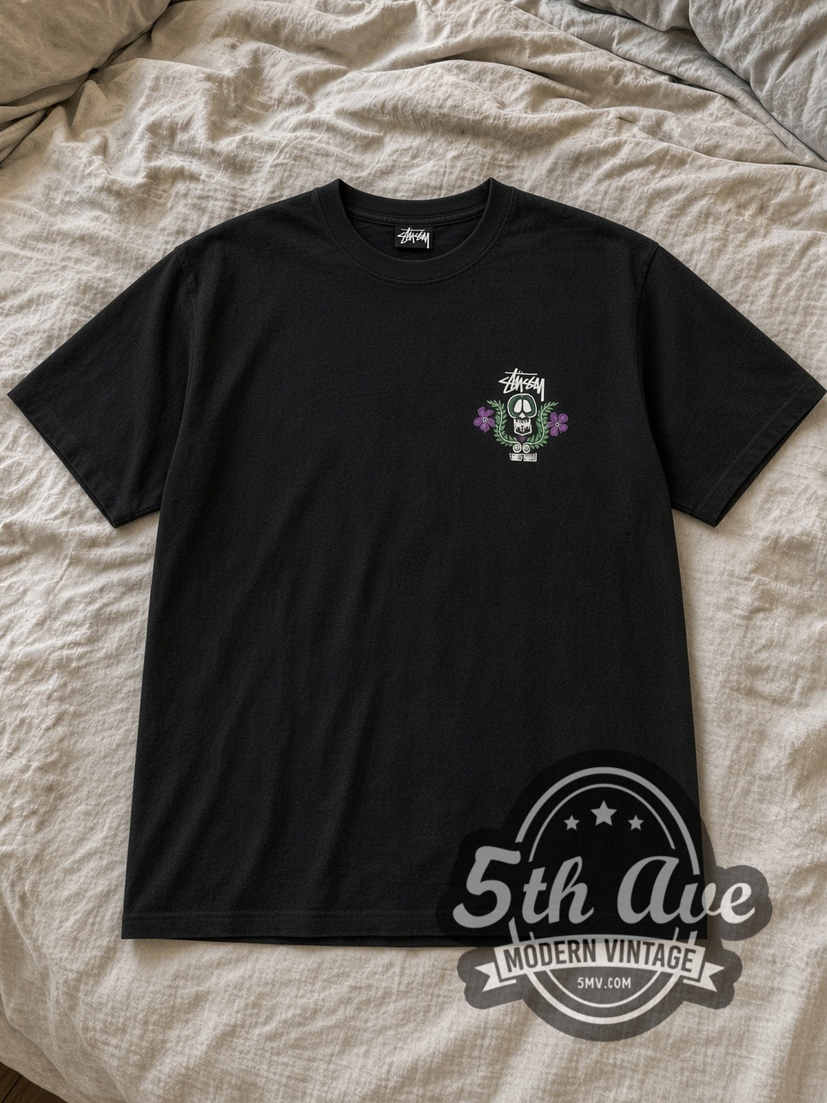 Black Stussy World Tribe Skull Crest Vintage Graphic T-Shirt laid flat on a linen bed